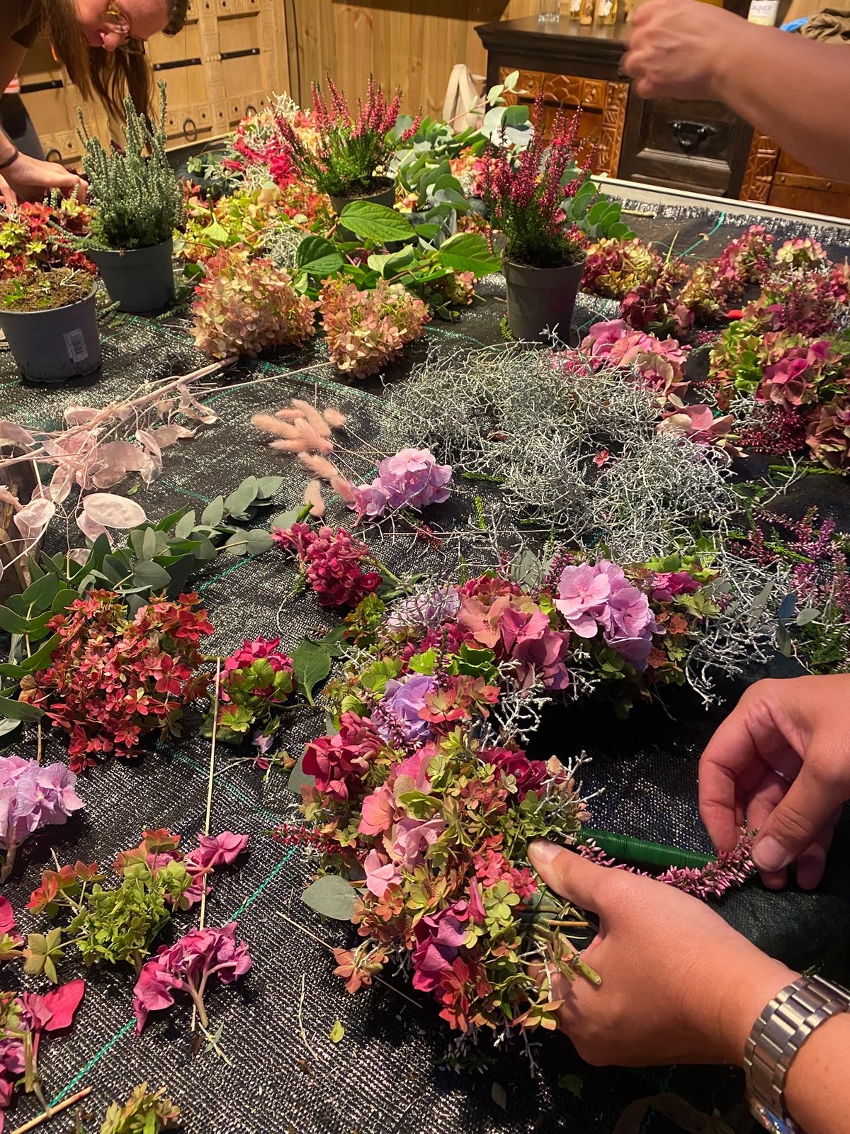 Hände beim Binden eines Kranzes mit rosa Hortensien